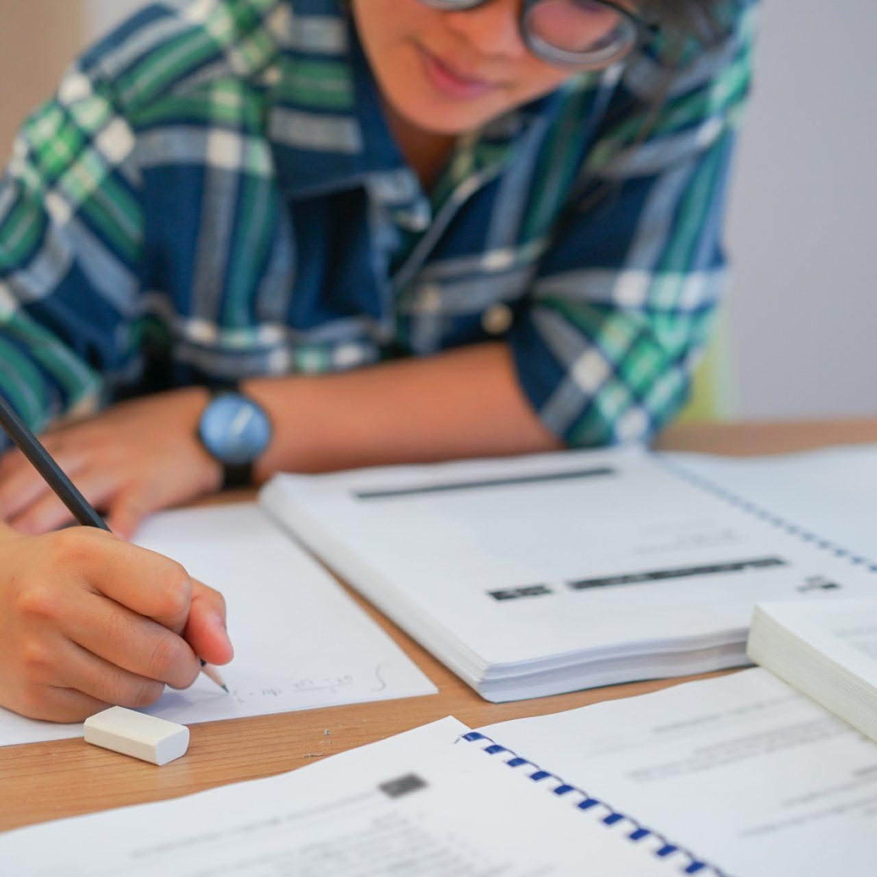 close up young asian student girl using pencil for writing formula of calculus on paper for do homework in library silent zone with textbook , campus lifestyle concept